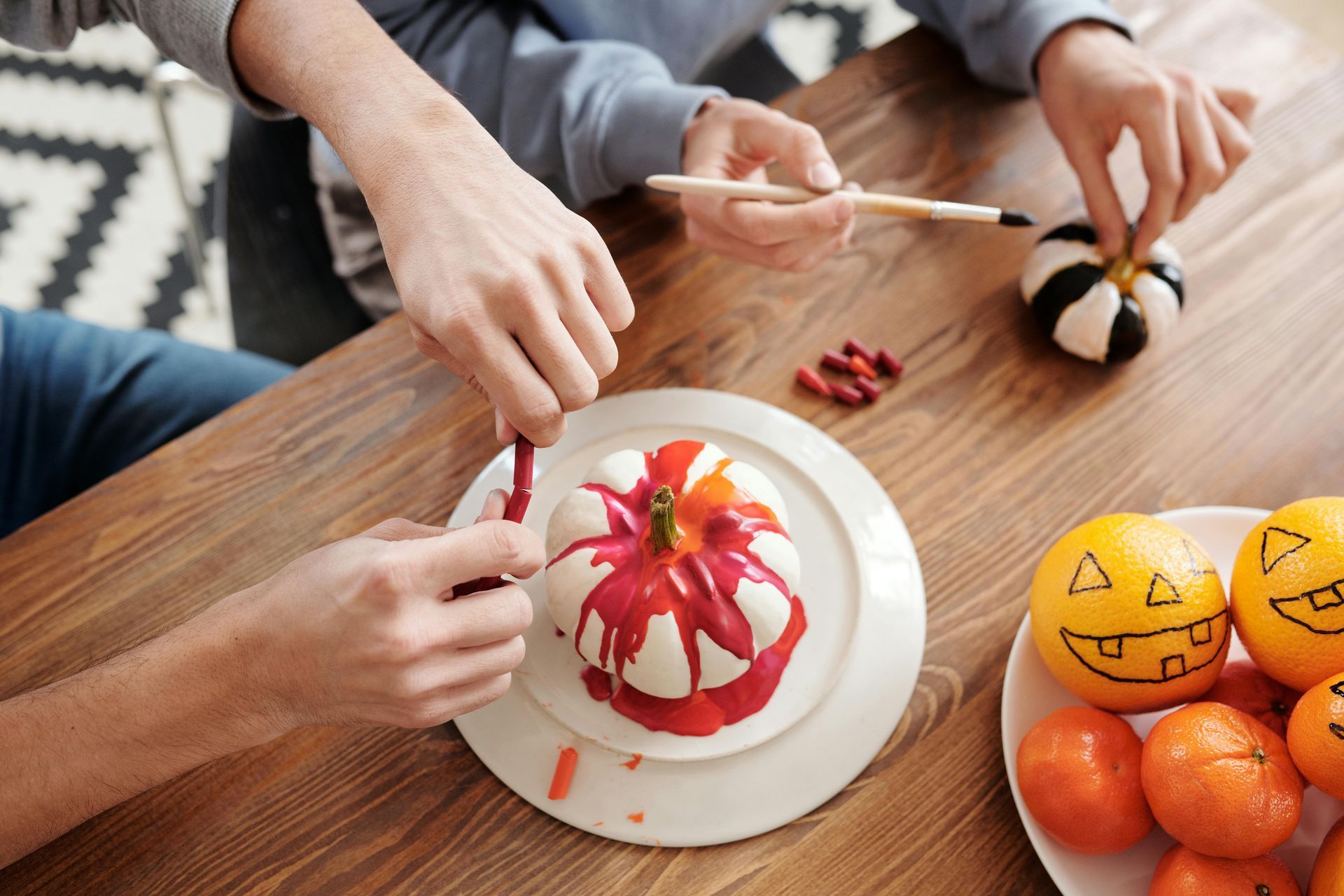 Invite your roommates or neighbors to a DIY night! Hands painting and melting crayons onto pumpkins, with jack-o'-lantern oranges nearby.