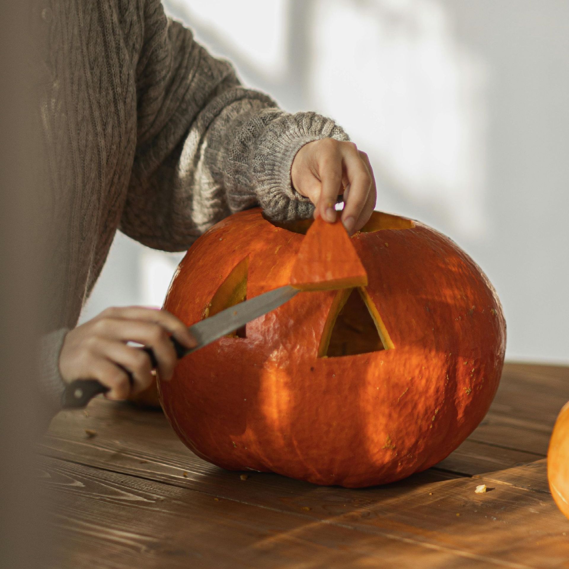 Hands carving a jack-o'-lantern, holding a freshly cut eye piece.