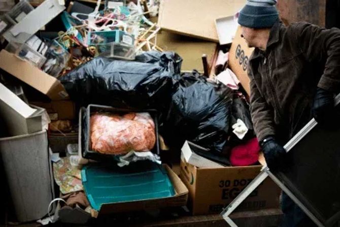 Man sorting through a large pile of household junk and trash and bags.