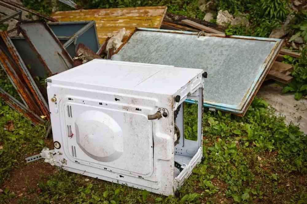 Old white washing machine discarded in a grassy junk pile.
