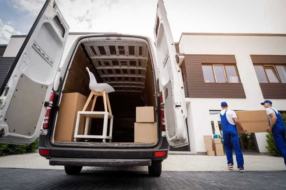Movers loading furniture and boxes into the back of a white van during an estate cleanout.