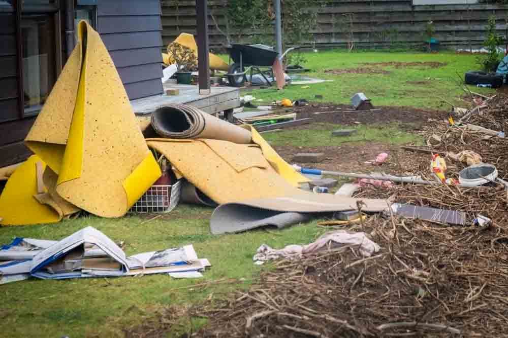 Discarded yellow carpet and outdoor debris on a residential lawn.