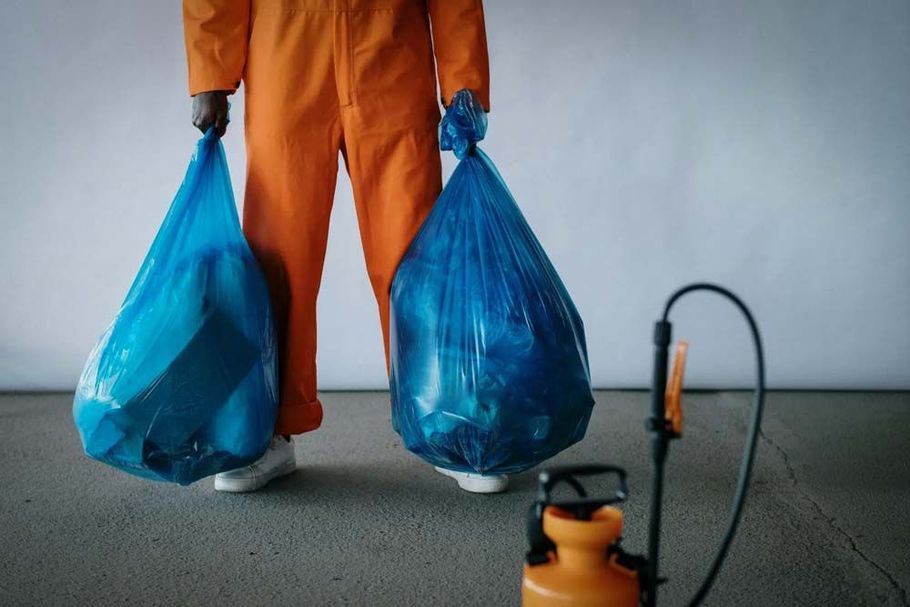 Garbage removal with a person in orange jumpsuit holding two large blue trash bags.