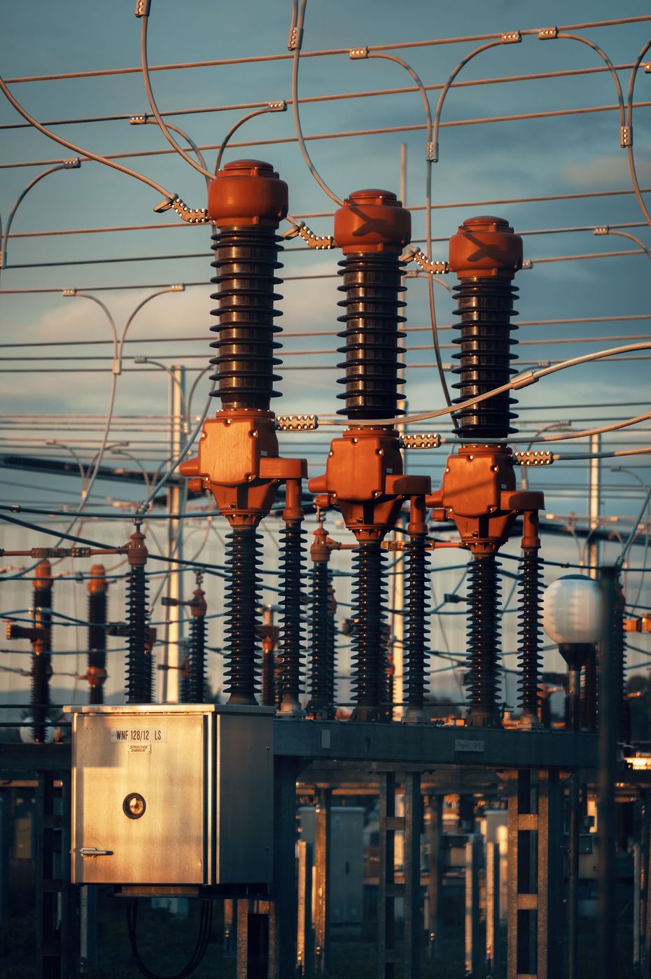 Utility workers in yellow helmets repairing power lines from bucket trucks against a blue sky