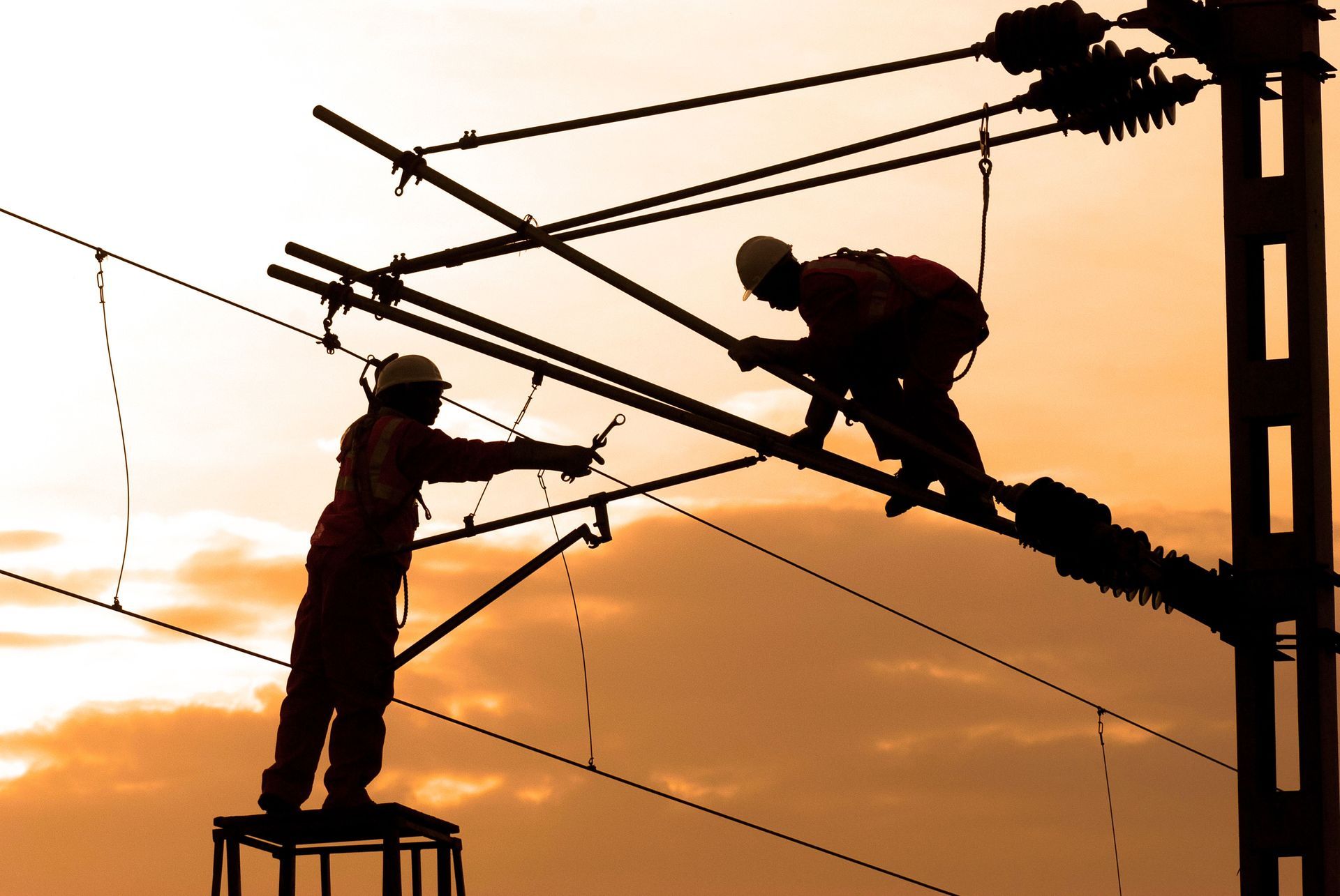 Utility workers in yellow hard hats repairing power lines from bucket trucks