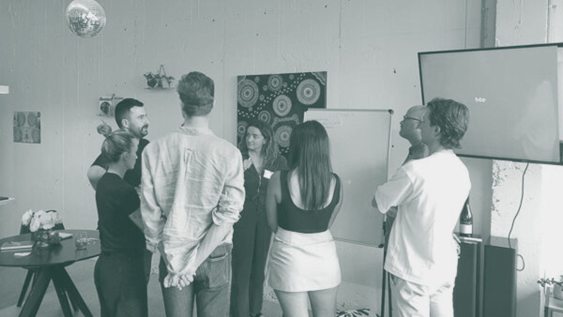 Woman holding award and certificate, smiling, is congratulated by a man. They stand indoors near art and a fan.