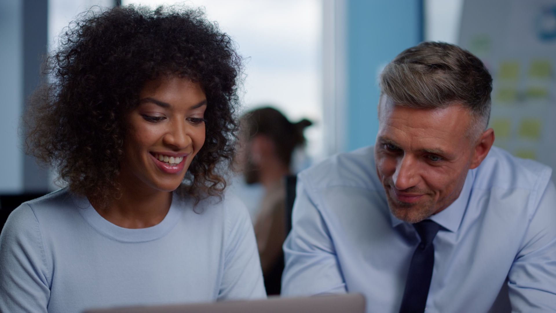 Woman and man smiling at a laptop screen in a modern office setting.