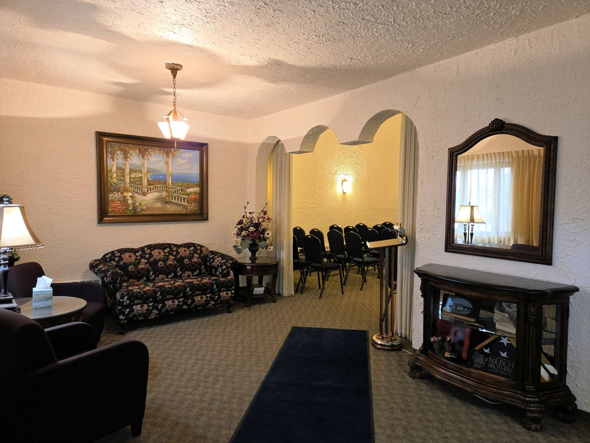 Funeral home interior: rows of chairs face a curtained stage, warm lighting.