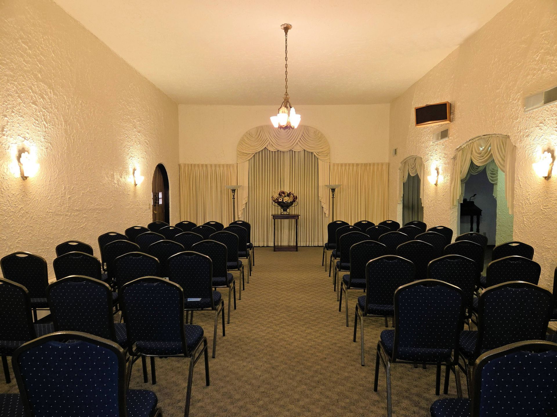 Interior of a waiting room with floral sofa, chairs, artwork, and cabinet with flowers and mirror.