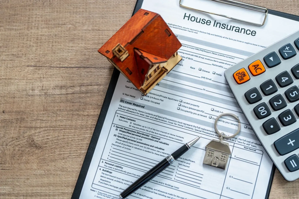 House insurance paperwork with a toy house, calculator, pen, and house key on a wooden table. House insurance paperwork with a toy house, calculator, pen, and house key on a wooden table.