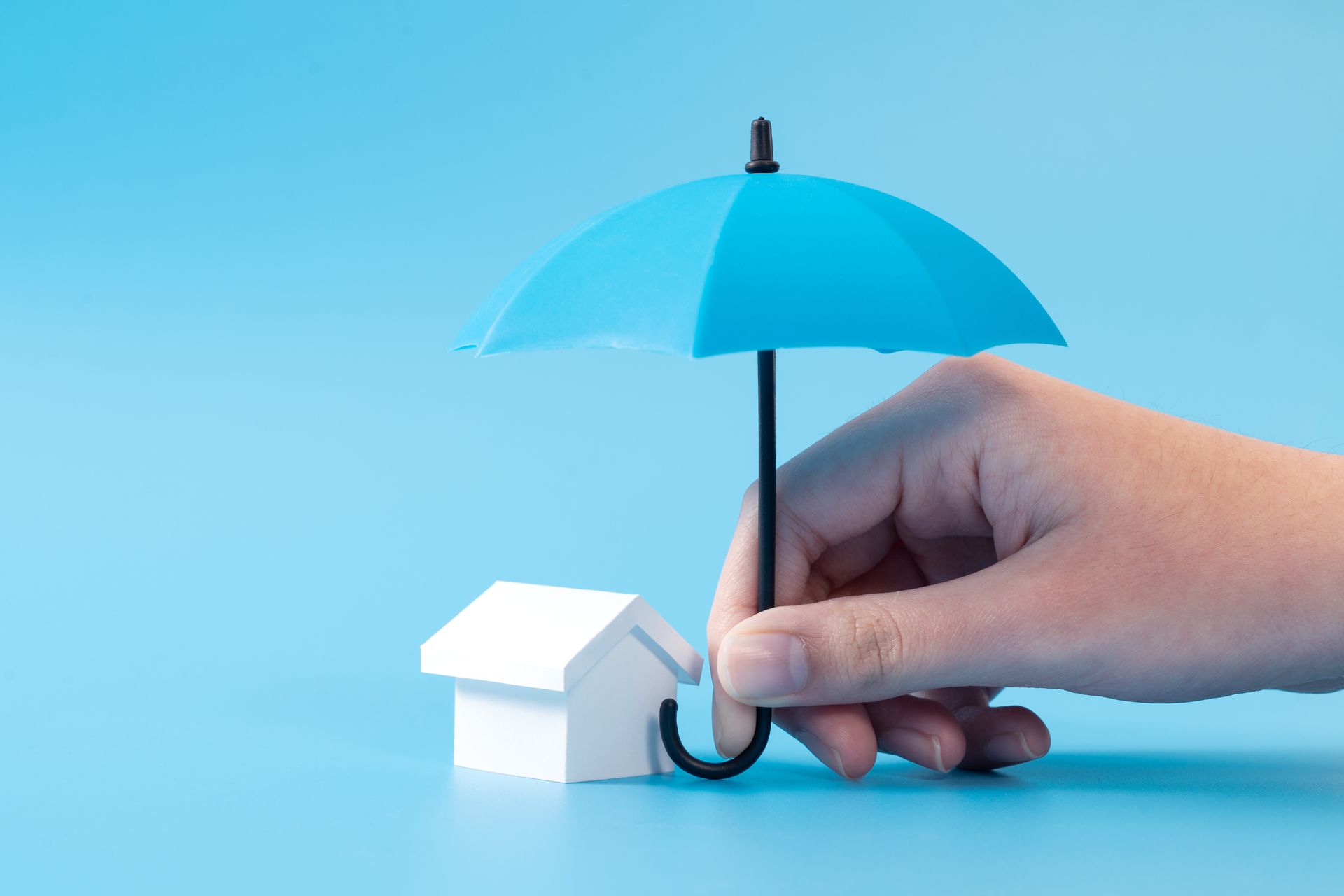A hand holds a small blue umbrella over a white house, with a blue background.