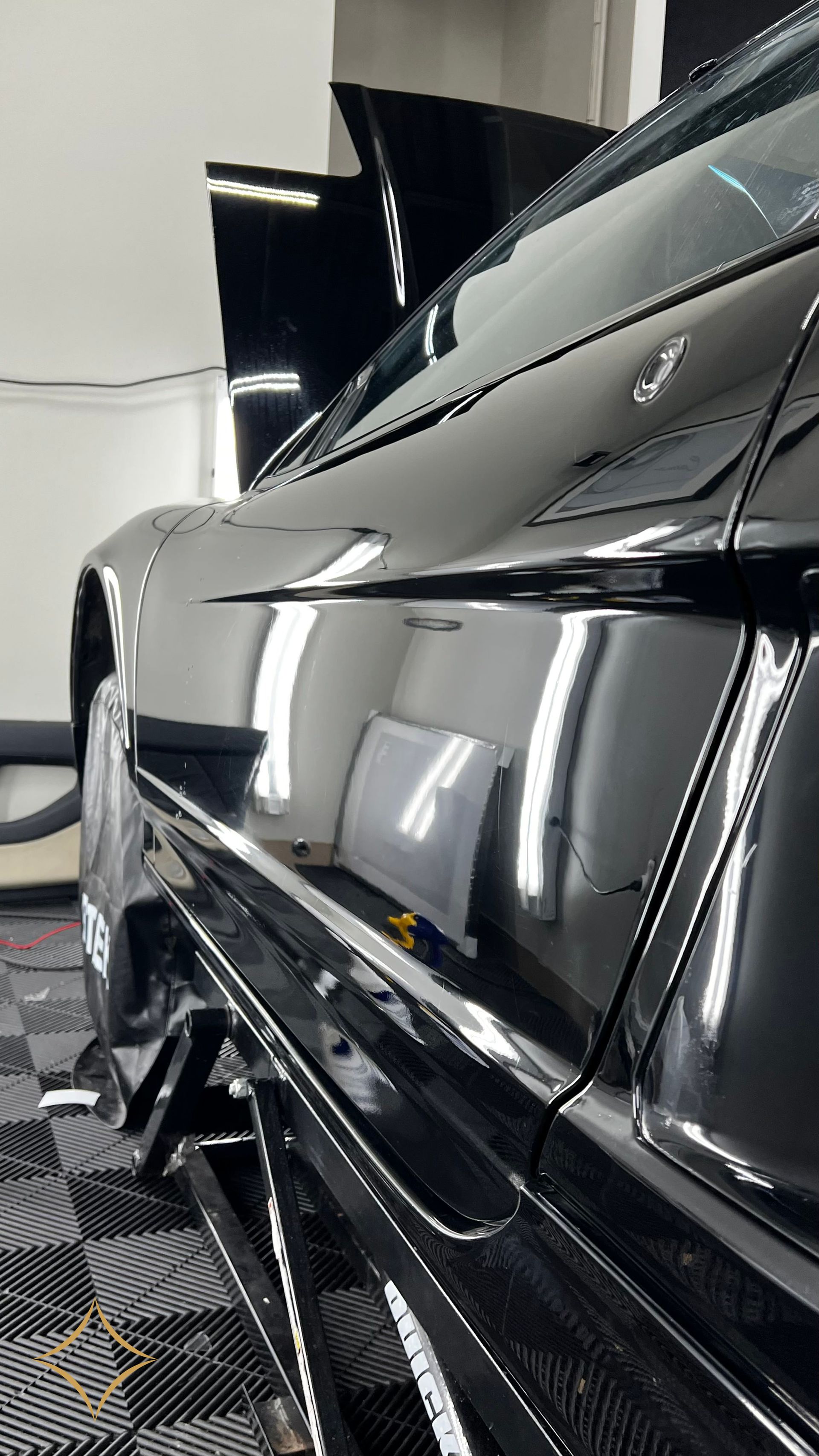 Black car side panel reflecting lights in a professional detail shop.