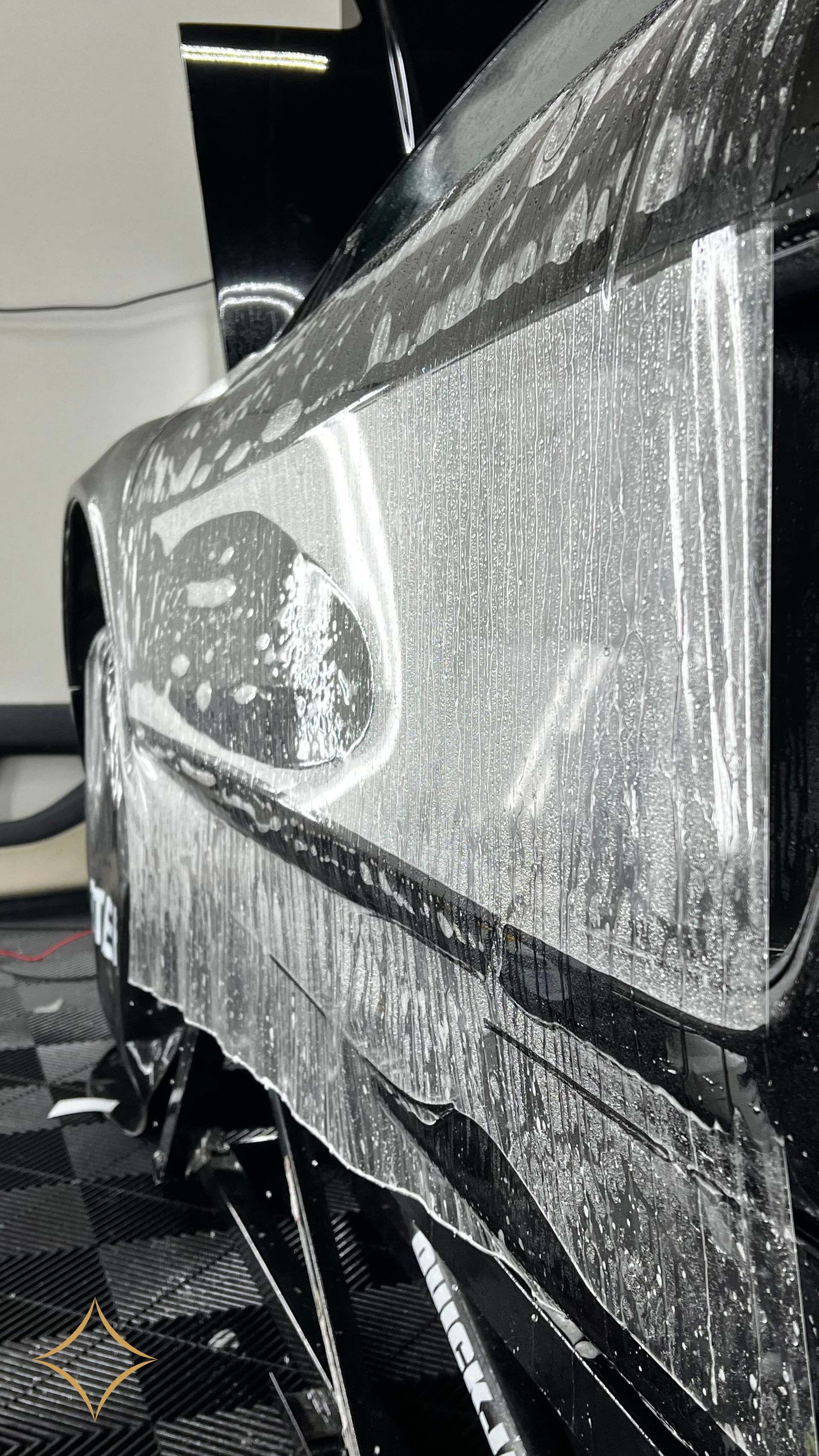Black car side covered in soapy water, being cleaned in a shop.