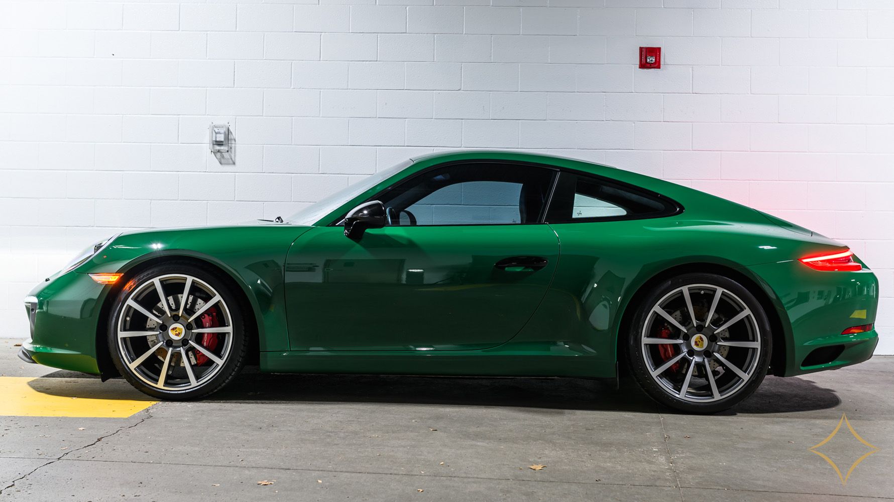 Green Porsche sports car parked in front of a white wall.