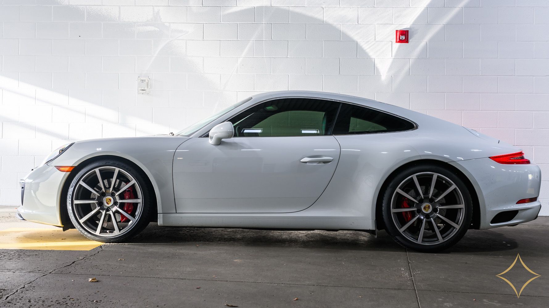 White Porsche sports car parked in a garage with grey and white walls and red brake calipers.