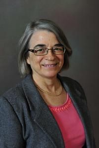 A woman wearing glasses and a pink shirt is smiling for the camera.