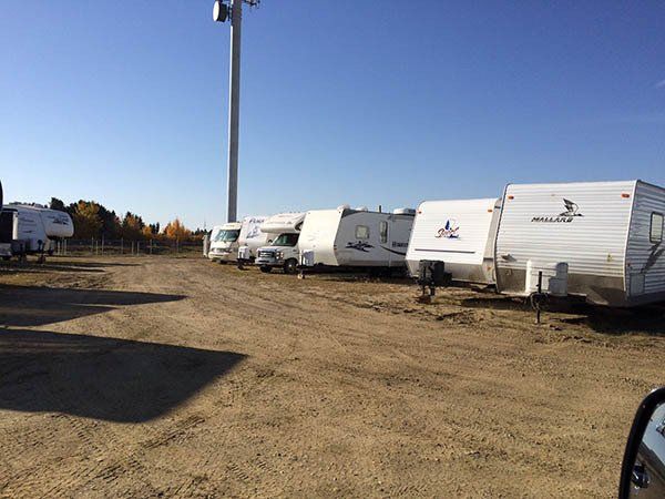 RVs and trailers parked in a dusty lot under a clear blue sky, with a tall light pole nearby