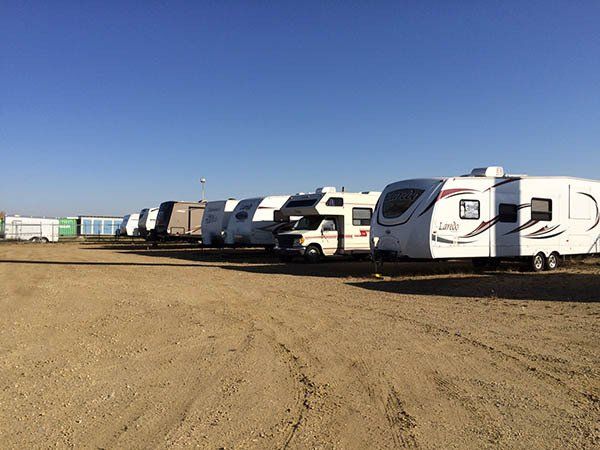 Row of white RV trailers parked on a dirt lot under a clear blue sky