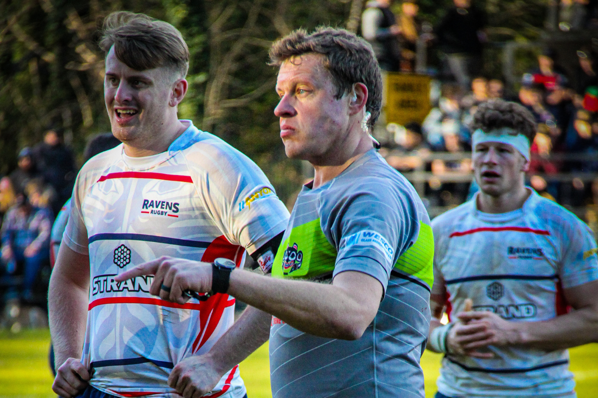Three rugby players in white and blue jerseys stand on a field after a match.