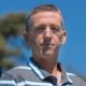 Portrait of a man in a striped polo shirt outdoors against a blurred blue background