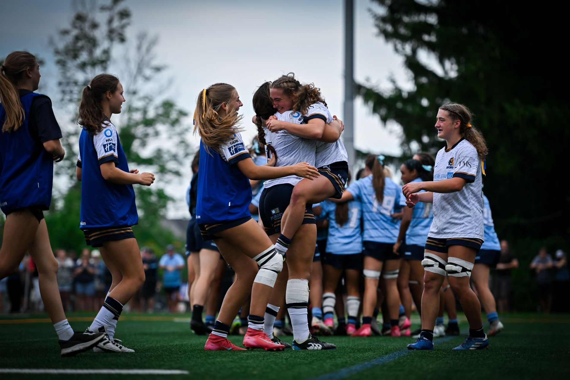 Soccer players in blue and white uniforms celebrate on a field after a match