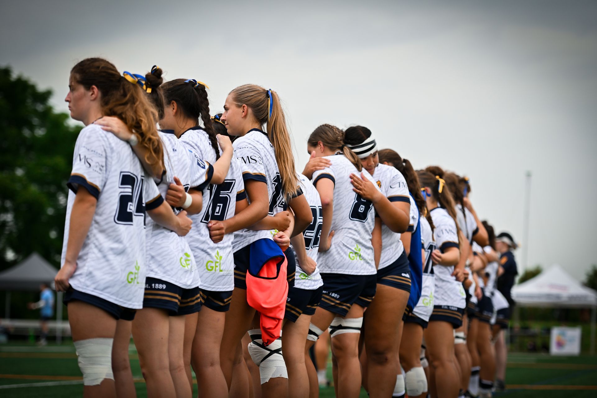 Soccer players in white jerseys stand in a line on a field, facing away during a pregame moment.