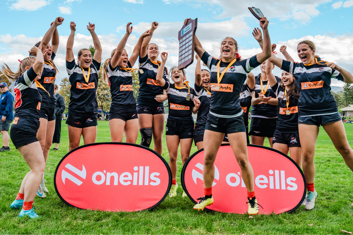 Sports team celebrating on a field with arms raised behind O’Neills sponsor boards
