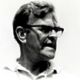 Black-and-white portrait of a man with glasses, looking to the side and smiling slightly.