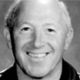 Black-and-white headshot of a smiling bald man against a dark background