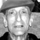 Black-and-white close-up of a man wearing a hat, looking directly at the camera