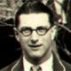 Black-and-white headshot of a man wearing glasses and a suit, facing forward with a neutral expression