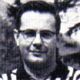 Black-and-white headshot of a man wearing glasses, looking at the camera.