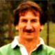 Smiling man in a green jacket outdoors against a blurred background