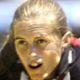 Close-up of a focused athlete with blonde hair, wearing a dark jacket, outdoors in bright sunlight