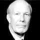 Black-and-white portrait of a bald man in a suit and tie against a plain background