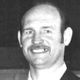 Black-and-white portrait of a smiling man with a mustache against a dark background