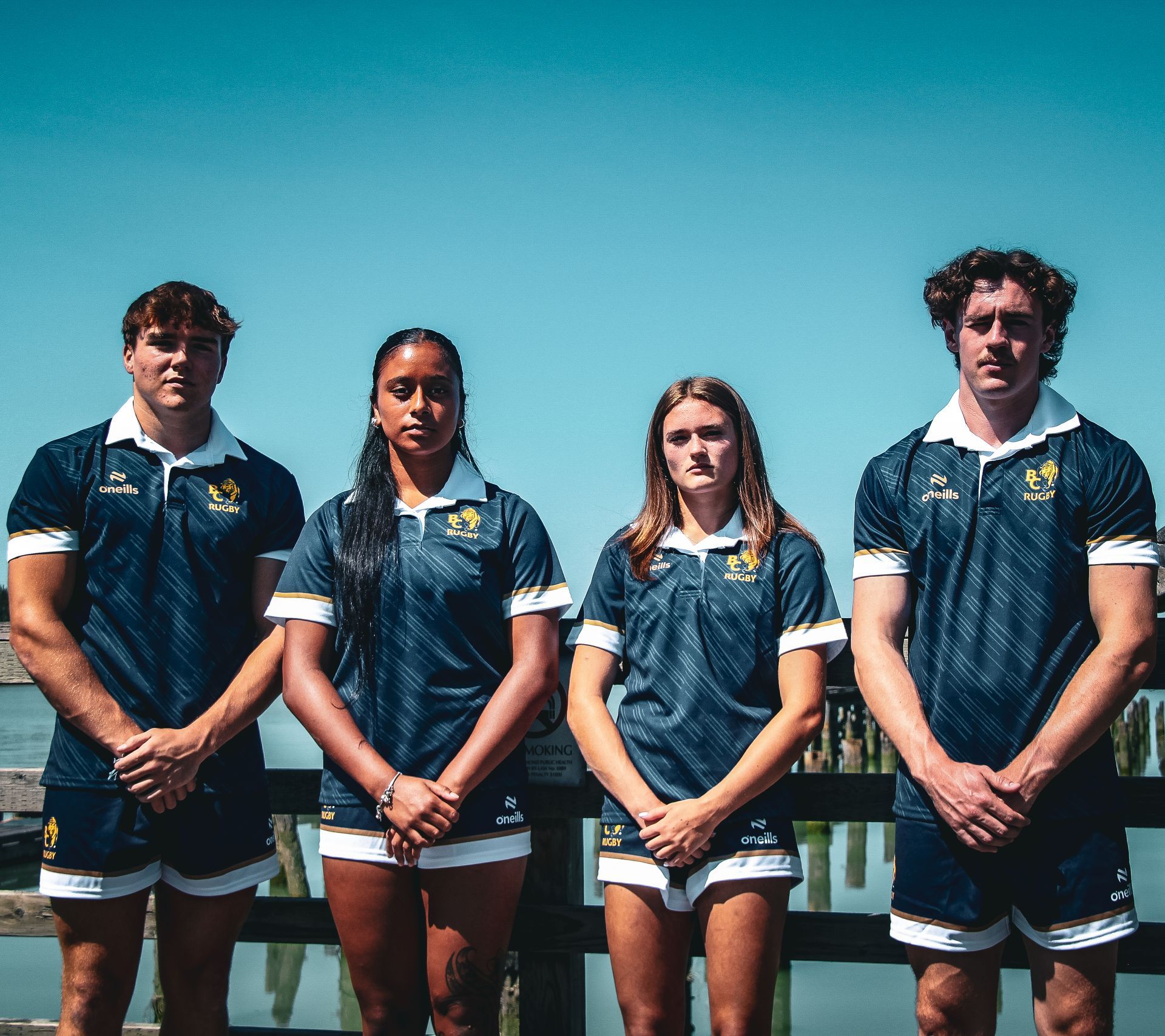 Four athletes in blue uniforms standing together outdoors under a clear sky