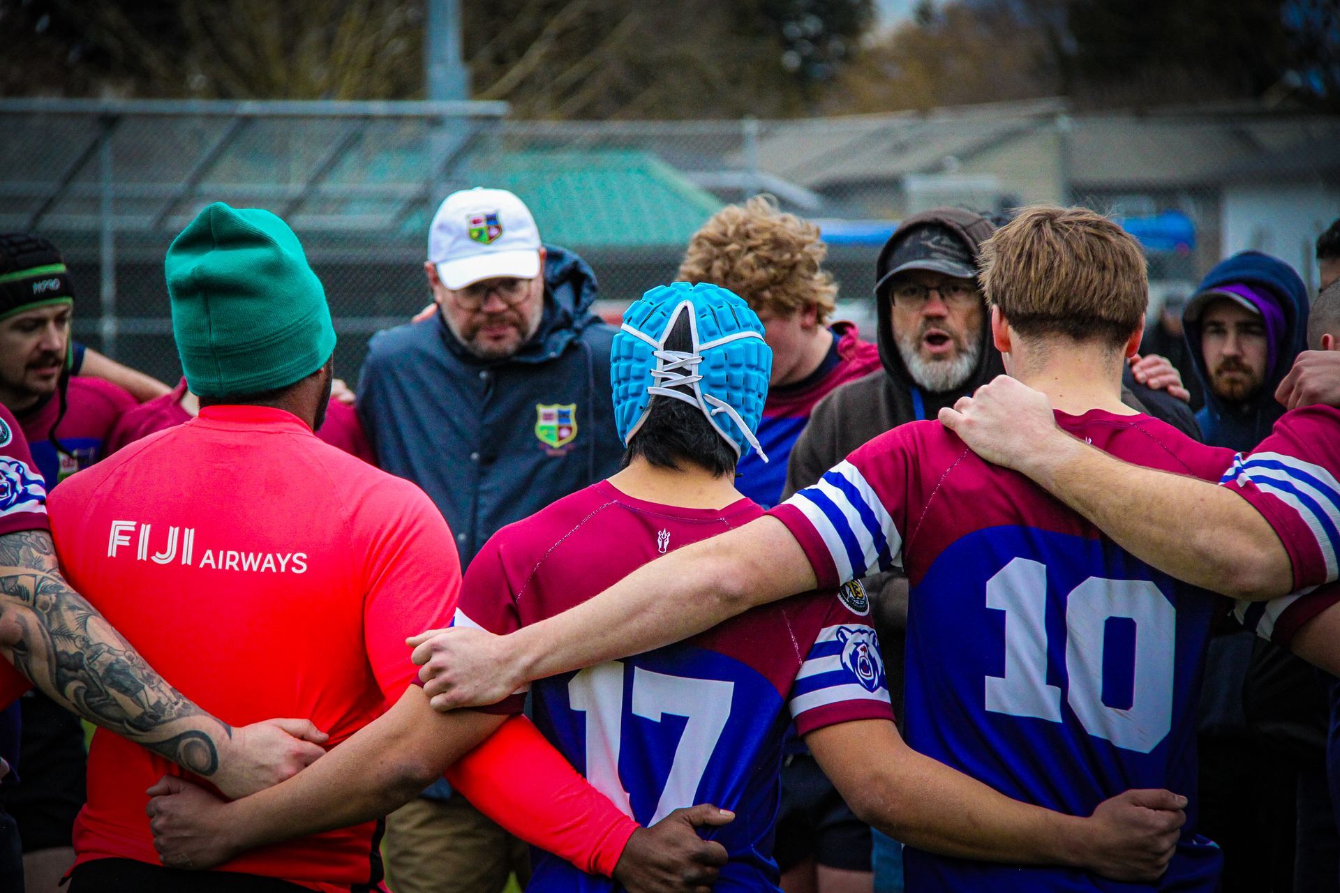 Rugby players in colorful jerseys huddle together on a field before a game