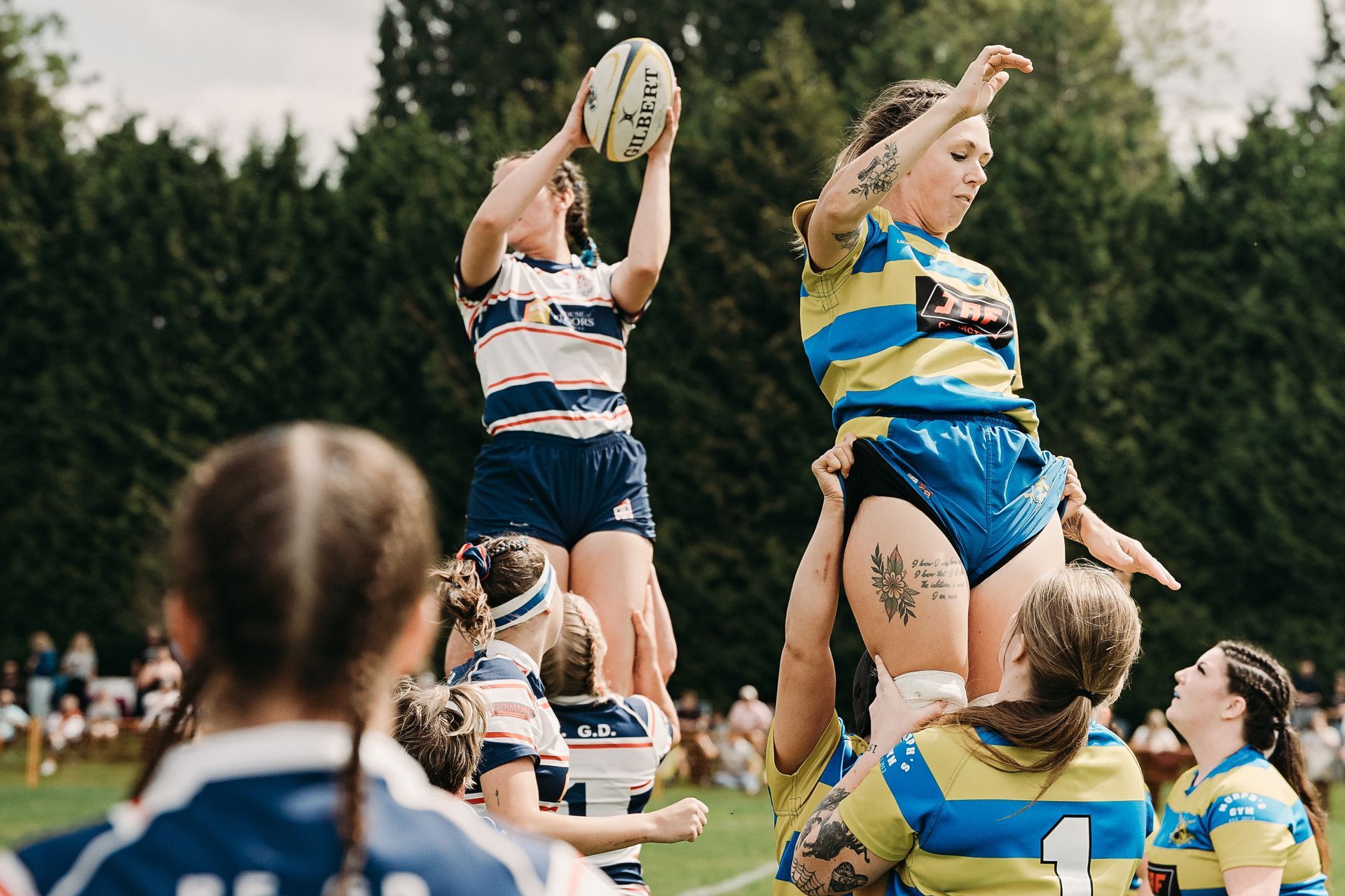 Rugby players in striped and blue jerseys jump to catch the ball during a match outdoors