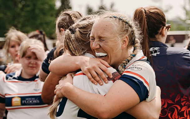 Rugby players in navy-and-red uniforms embrace and smile after a match