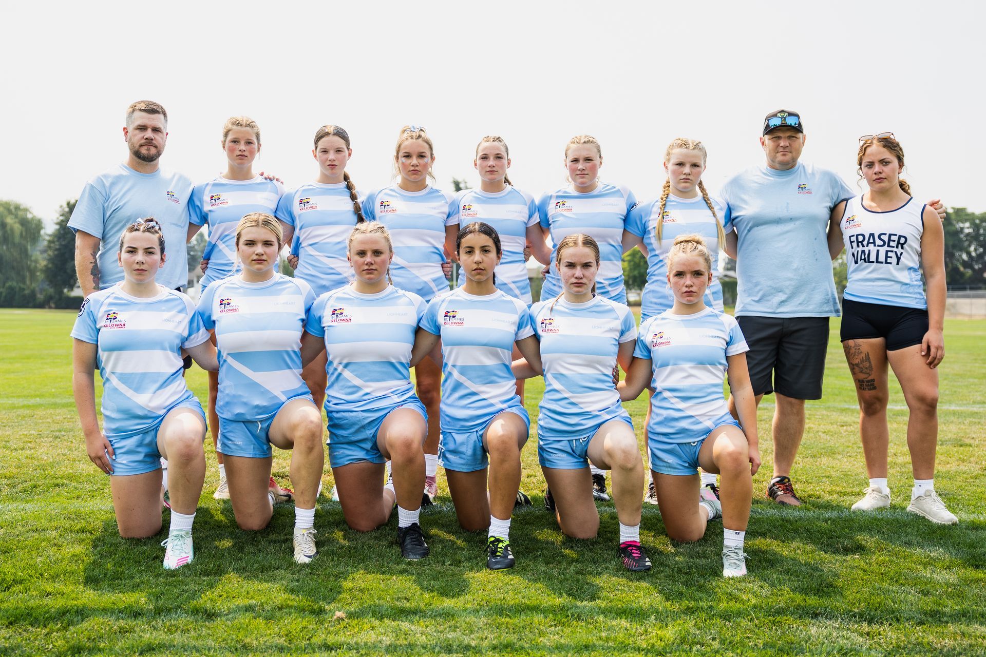 Youth sports team and coaches posing on a grassy field, wearing blue and white uniforms.