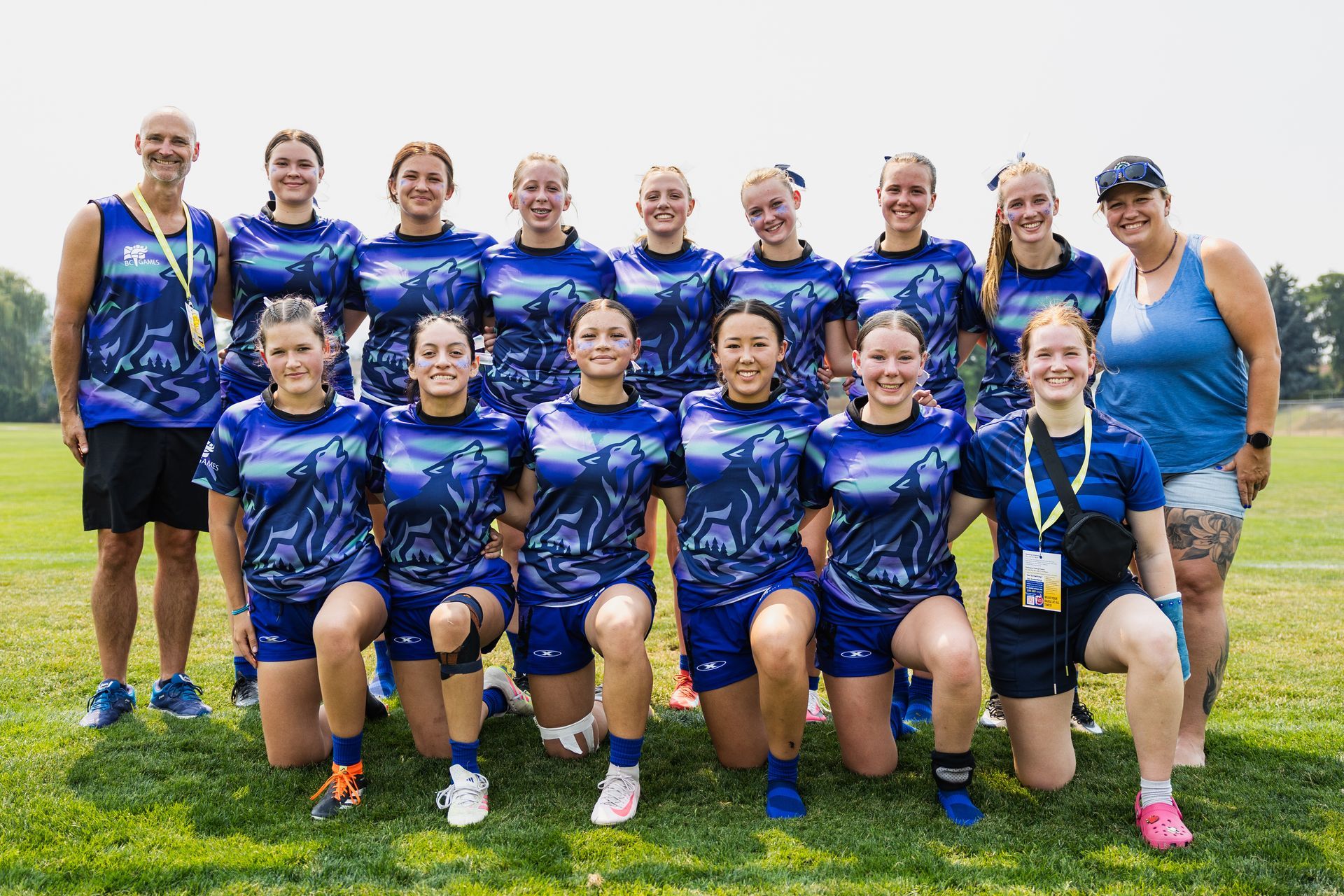 Group of athletes in blue uniforms posing on a grassy field at an outdoor event