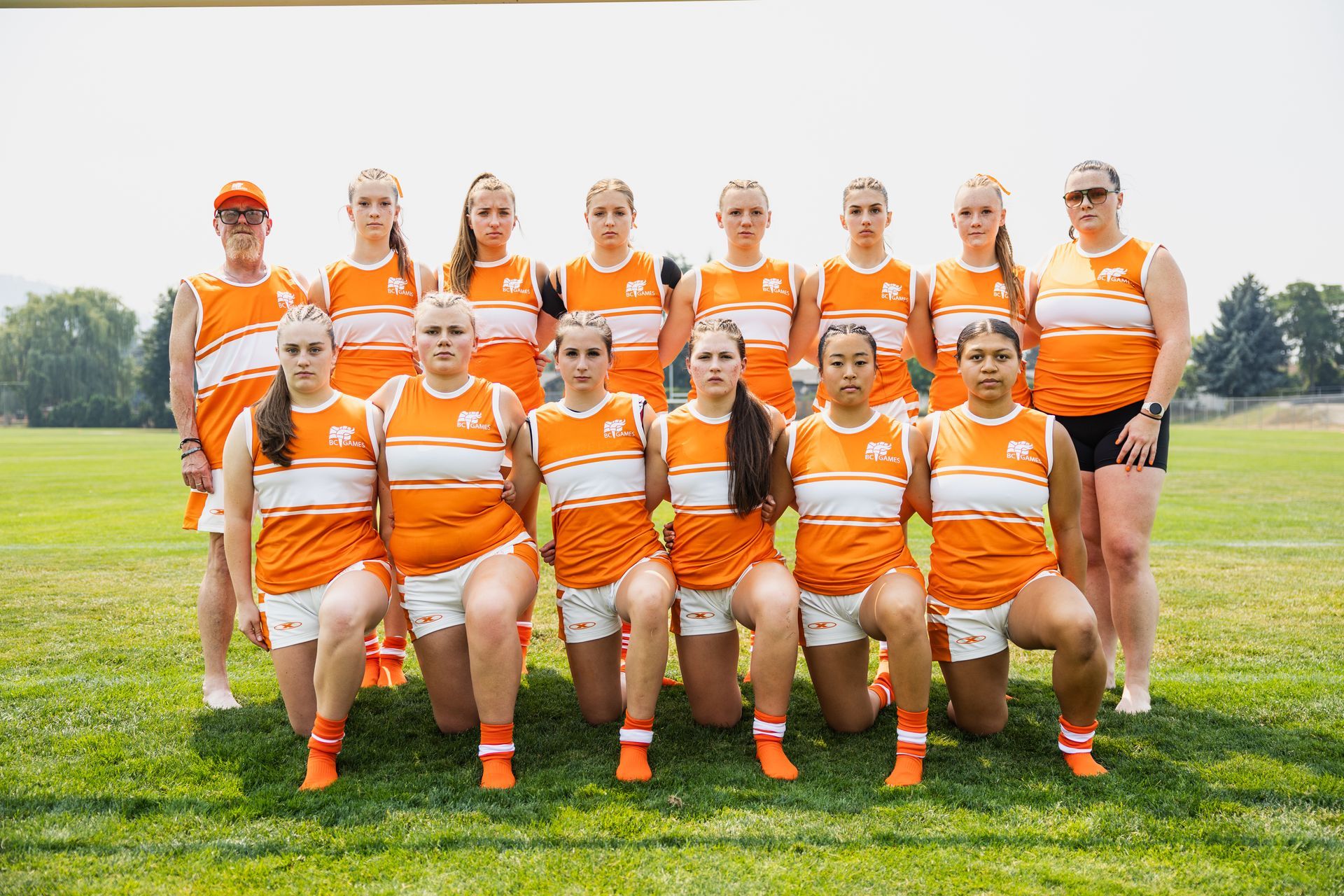 Softball team in orange-and-white uniforms posing on a grassy field outdoors