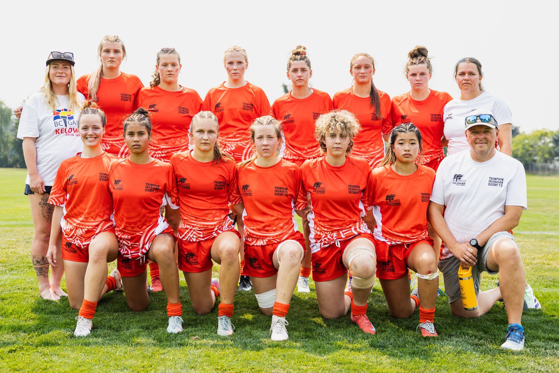 Soccer team in orange uniforms posing for a group photo on a grassy field