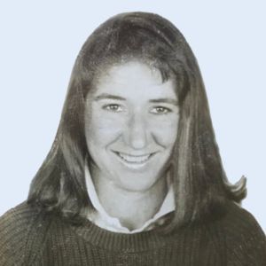 Black-and-white portrait of a smiling person with long hair wearing a dark sweater over a white collared shirt
