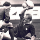 Black-and-white photo of two people lifting a child outdoors, with one person reaching up toward the child