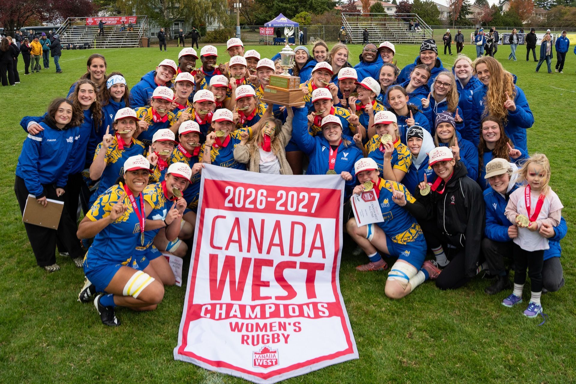 Group of youths and coaches posing on a grassy field with a red “Canada West Champions” banner