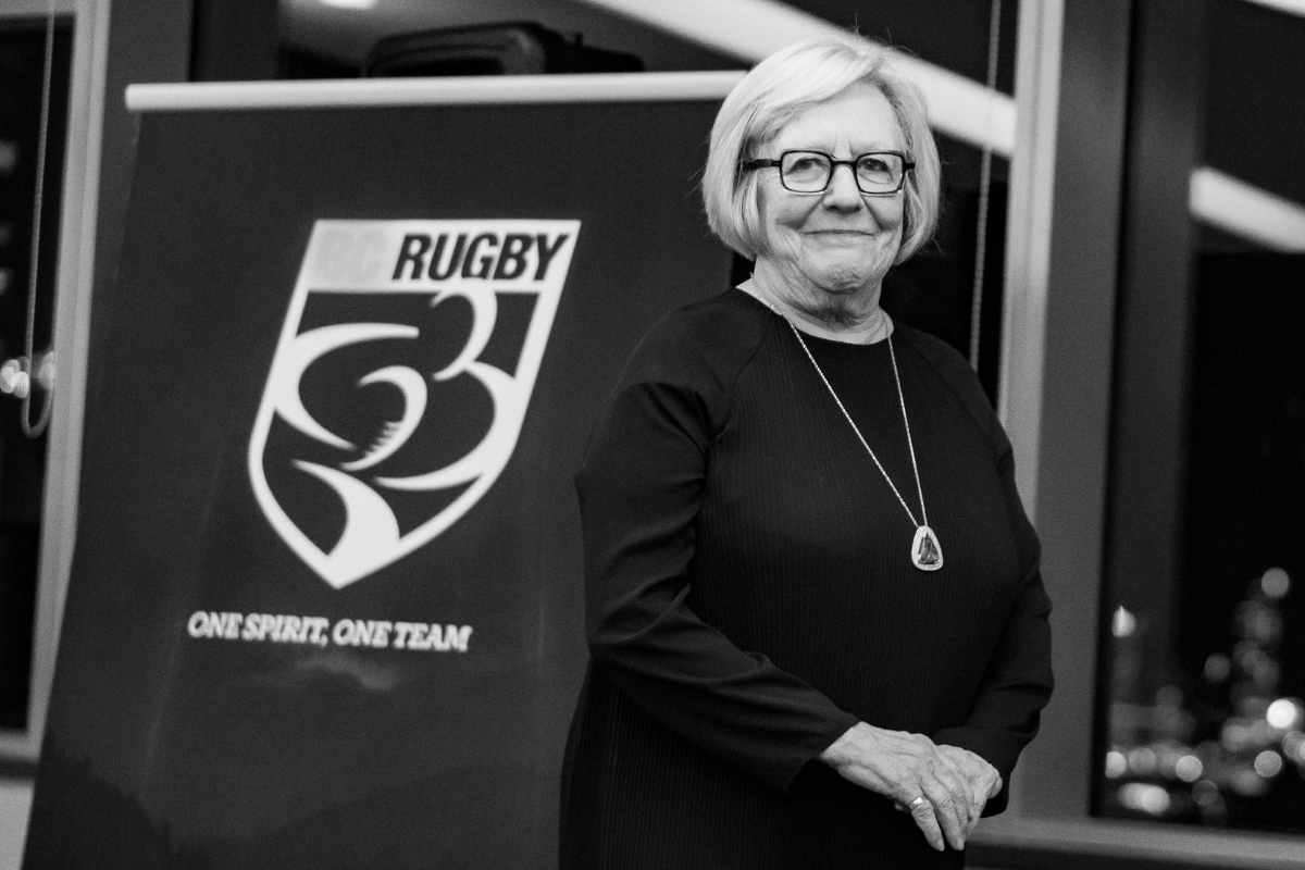 Woman standing beside a Rugby 3 banner, smiling in a black-and-white indoor setting.