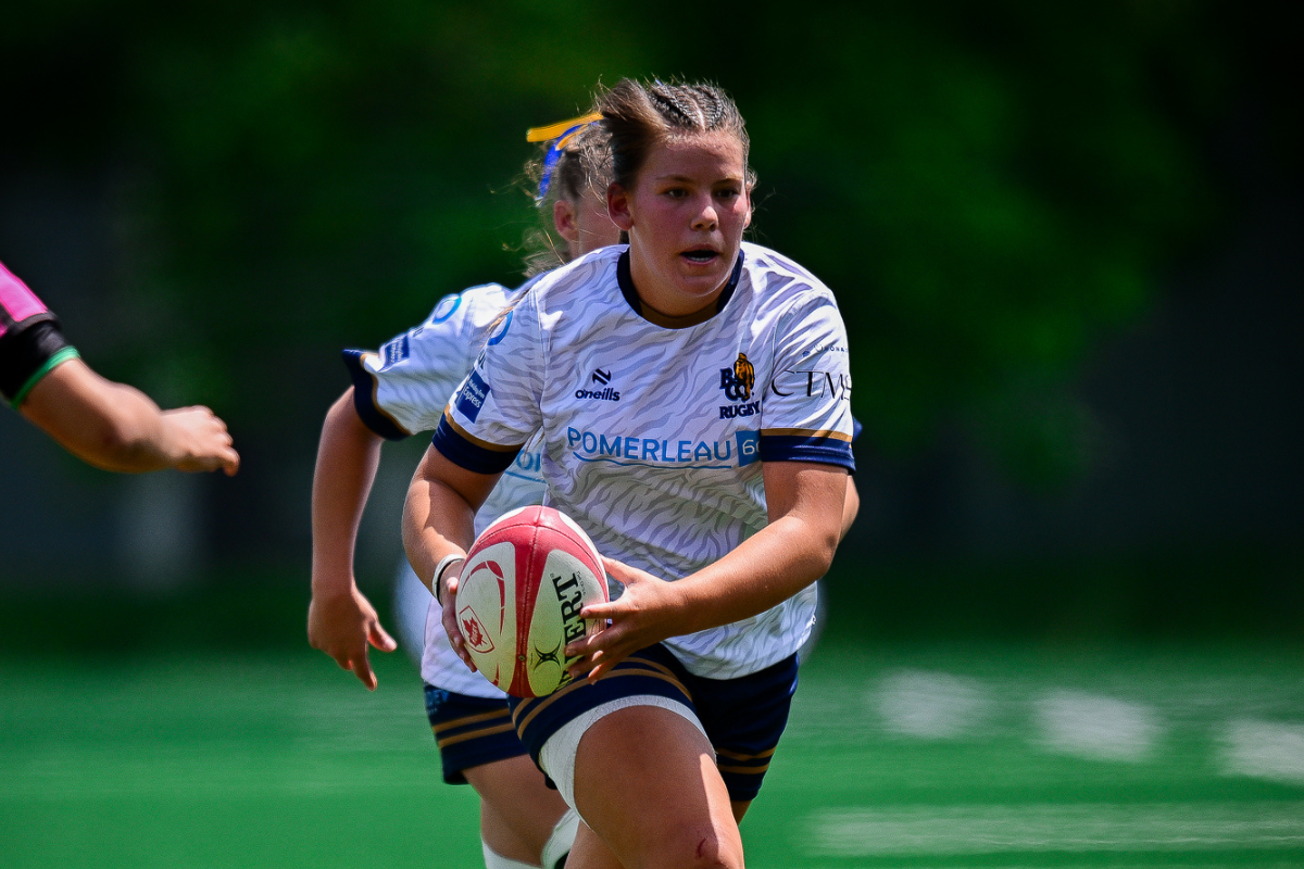 Rugby player in white and navy jersey runs with the ball on a green field