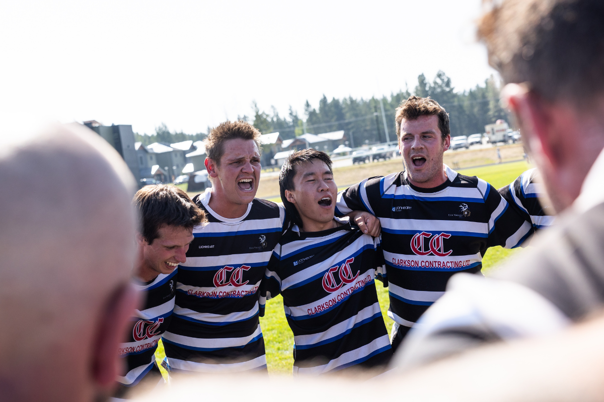 Rugby players in black-and-white striped jerseys huddle and cheer on the field.